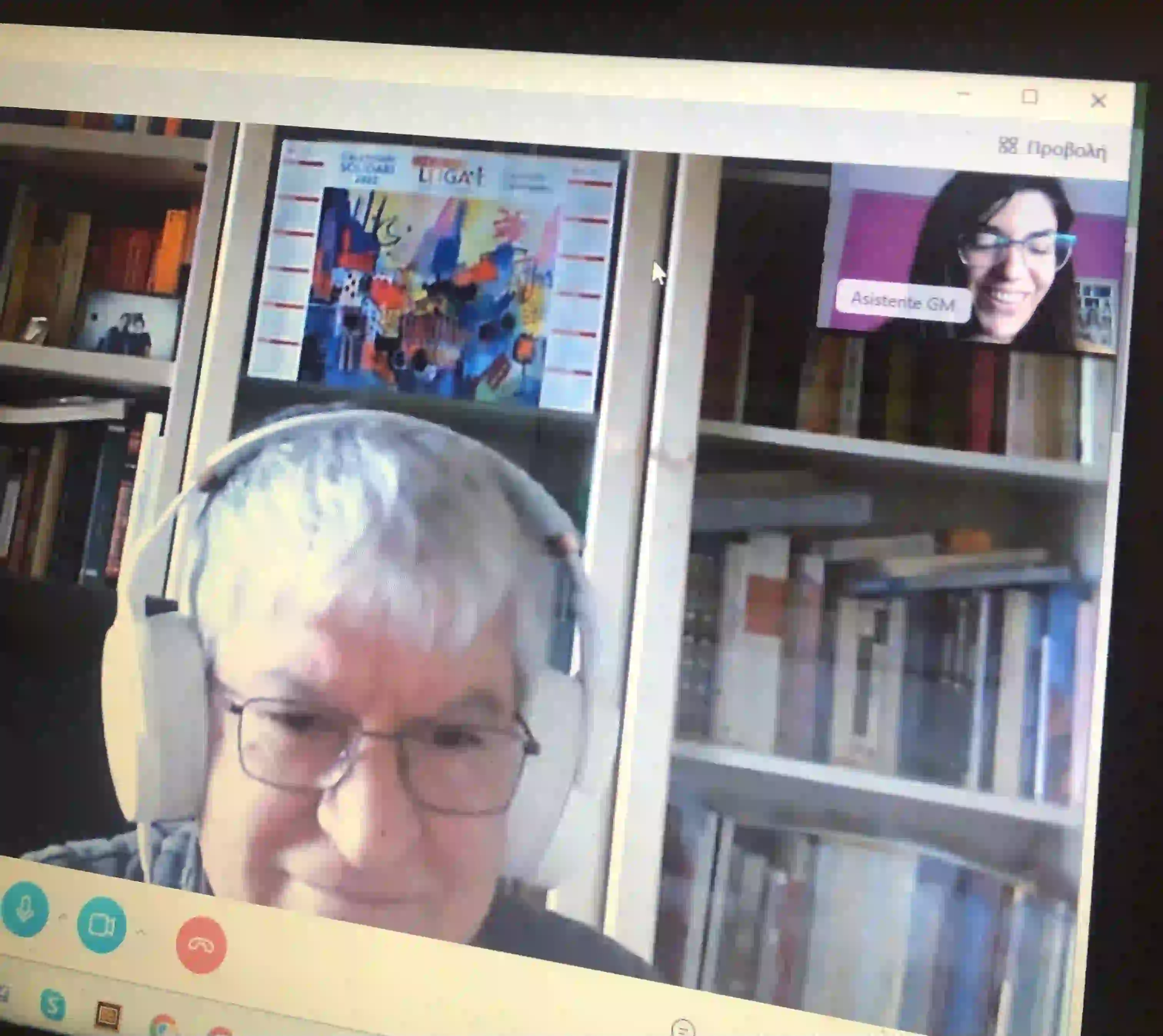 An older student in headphones on a Skype Greek lesson, bookshelves behind