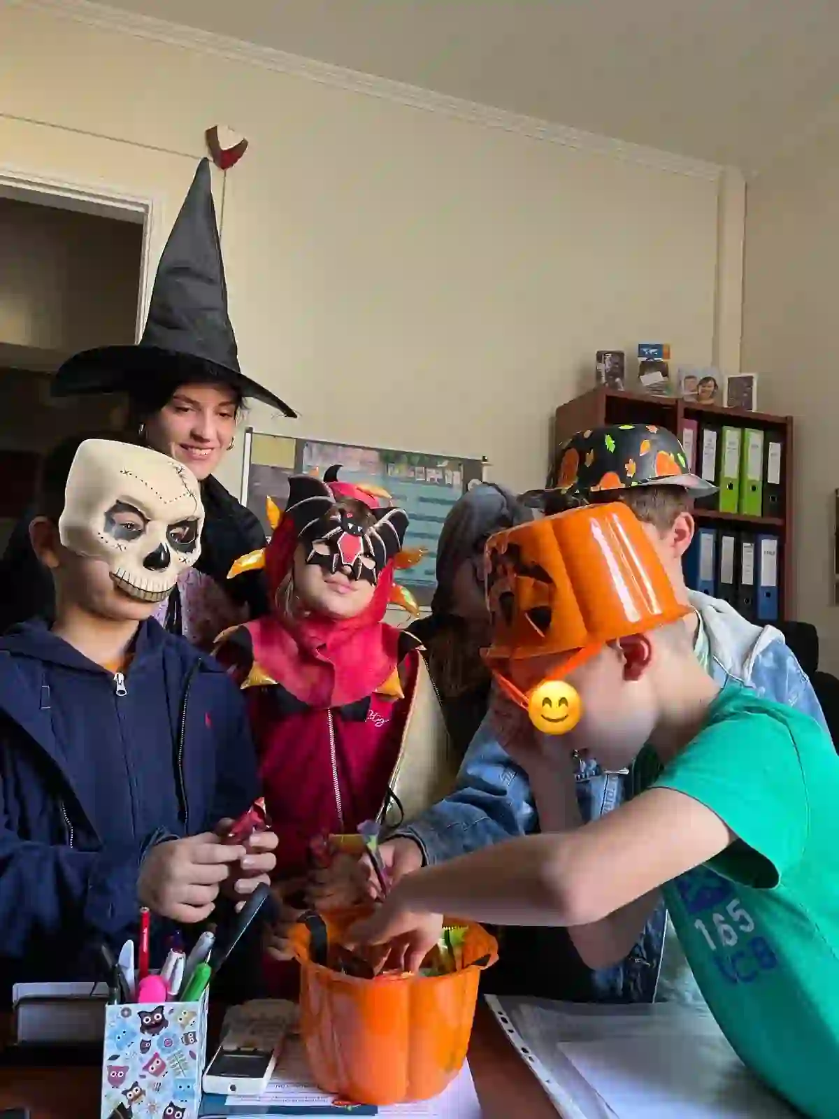 Kids in Halloween costumes and masks digging into a pumpkin treat bucket in class
